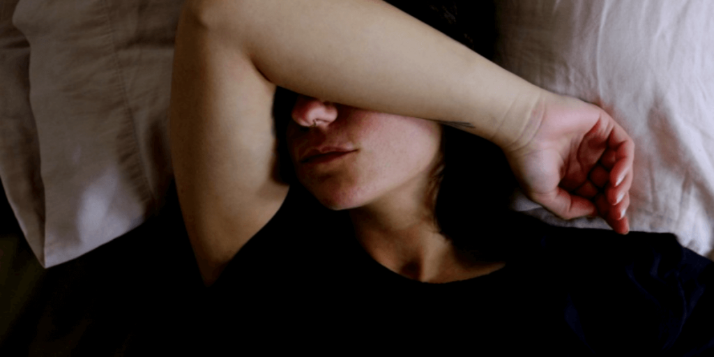 갑상선 기능 저하증 때문에 침대에 누워 오른팔을 이마에 얹어 누워있는 여성
