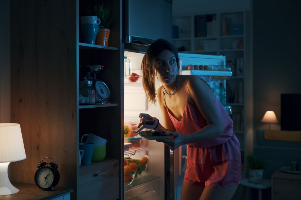 불 꺼진 주방에 여자가 잠옷차림으로 냉장고 문을 열고 몰래 먹는 모습